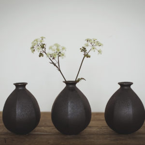 Group of three black faceted vases with a dried stem of foliage in the middle vase