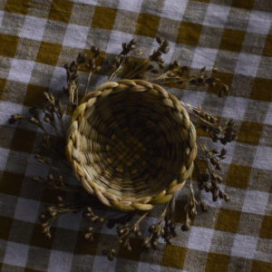 miniature woven basket with seed heads woven around the rim. Shown on a green and white gingham cloth