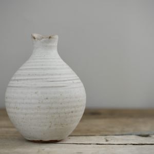 pale stoneware budvase shown on a rustic wooden tabletop against a light grey background.