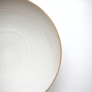 Inside of a white stoneware bowl showing the pattern of the inside where its been wheel thrown. Shown on an off-white background