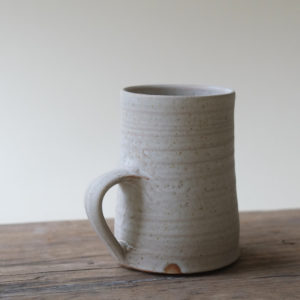 Simple stoneware mug with a flat, matt finish. Shown on a rustic wooden table against an off-white background