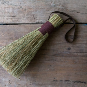 natural fibre hand brush bound with a brown cotton handle. Shown on a light, weathered table.