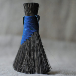 Indigo blue brush with dark fibres. Shown on an earthy coloured fabric backdrop.