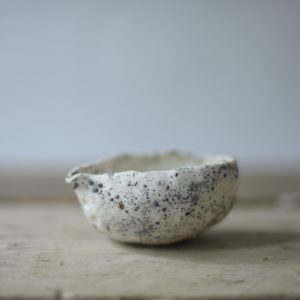 a small white and grey, heavily textured pouring vessel set against a white backdrop, on a rustic wooden board.