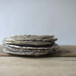stack of textured white and grey plates. Shown on a rustic wooden table against a white backdrop.