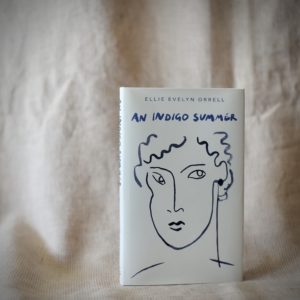 A hardback book with a white cover. Showing a blue ink line drawing of a face. Shown against a pale pink fabric backdrop.
