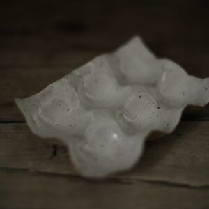 Speckled white stoneware egg holder suitable for six eggs. Shown on a rustic wooden farmhouse table