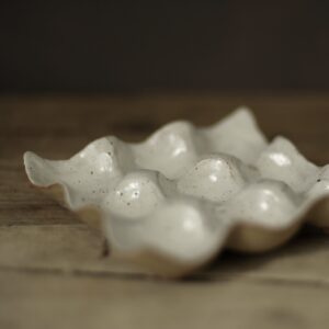 Speckled white stoneware egg holder suitable for nine eggs. Shown on a rustic wooden farmhouse table