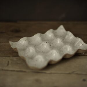 Speckled white stoneware egg holder suitable for twelve eggs. Shown on a rustic wooden farmhouse table