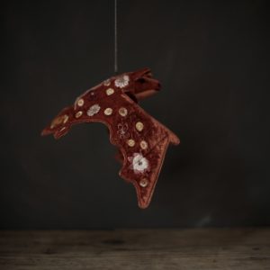 A dark rustic orange coloured fabric bat which has been embroidered with brightly coloured flowers. Shown hanging above a wooden table against a very dark background.