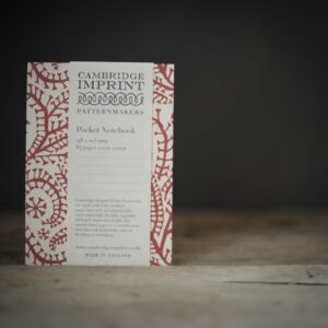A red and white paisley patterned notebook. Photographed on a rustic wooden table against a very dark brown background.