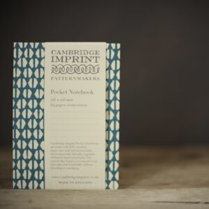 A greeny/blue notebook covered in crescent shaped white marks. Shown on a rustic wooden table against a dark brown background.