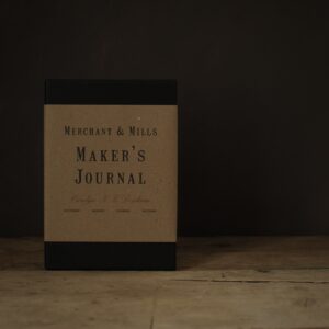 a black book with a brown paper belly band. Shown on a rustic wooden table top.
