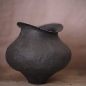Large bulbous black vase shown against a stone pink background.